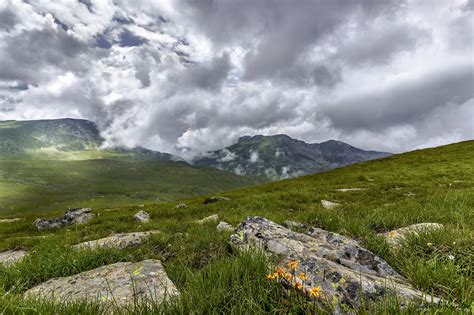 Green Grass Field With Rocks Near Mountains During Cloudy Daytime Sky