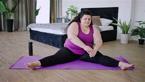 Young Overweight Woman Stretches Body Sitting On Mat At Home Stock