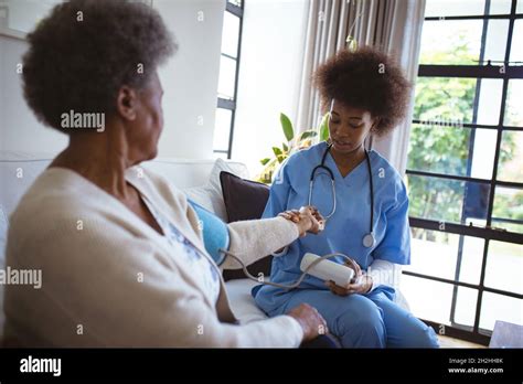 African American Female Doctor Treating Senior Female Patient At Home