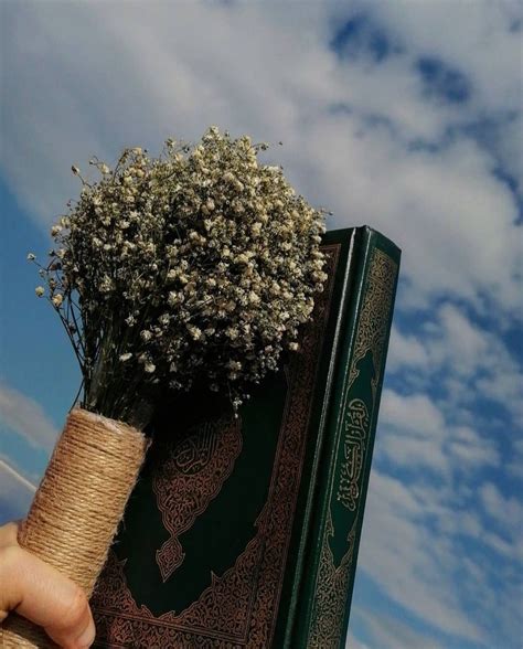 A Hand Holding A Book With Flowers In It And The Sky Is Blue Behind It