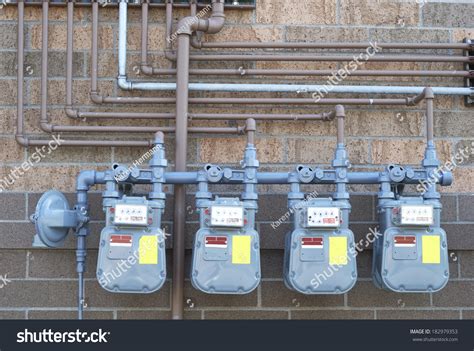 A Row Of Natural Gas Meters And Pipes Against A Two Toned Brick Wall
