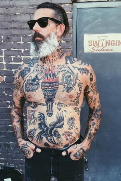 A Man With Lots Of Tattoos On His Chest Standing Next To A Brick Wall