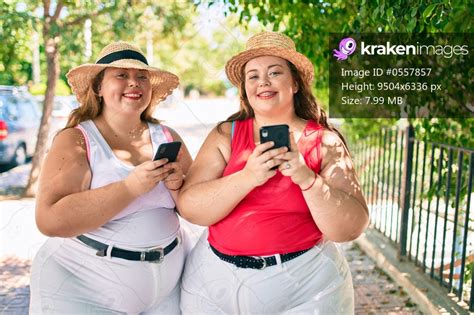 Two Plus Size Overweight Sisters Twins Women With Smartphone Outdoors On A Sunny Day Kraken Images