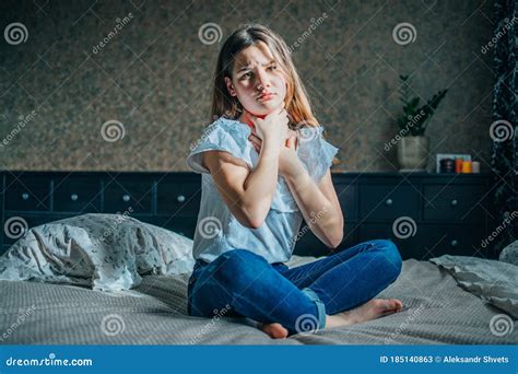 A Young Brunette Girl Sits On A Bed In Her Room She Has A Sore Throat She Squeezes Her Neck