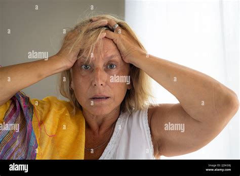 Caucasian Woman Between 50 And 60 Years Old With Blonde Hair And Both Hands Holding Her Head
