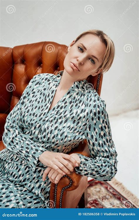 Serious Adult Woman With Short Hair Is Sitting In A Bright Room On A Leather Chair And Looking
