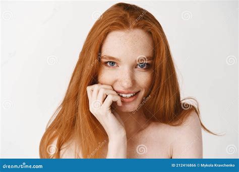 close up of flirty redhead woman with pale skin and no makeup biting fingernail and staring at