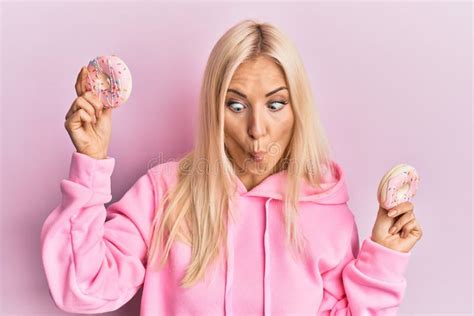 Young Blonde Woman Holding Tasty Pink Doughnuts Over Eyes Making Fish