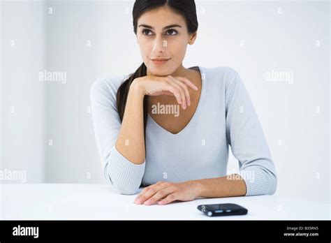 Woman Sitting At Table With Hand Under Chin Looking Away Stock Photo