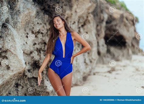 Beautiful Tanned Girl In Blue Swimwear Posing On Beach With Rock On