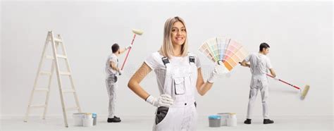 Female House Painter Holding A Color Palette And Male Workers Painting