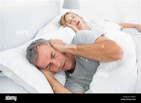 Tired Man Blocking His Ears From Noise Of Wife Snoring In Bedroom At