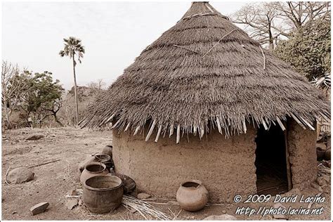 An Adobe Hut With Thatched Roof And Pots On The Ground In Front Of It