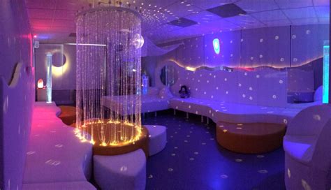 a room with white couches and purple lights on the ceiling is lit by colorful lighting