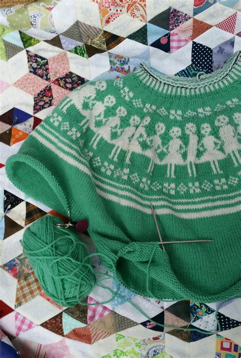 A Green Sweater With White Designs On It And Some Knitting Needles In
