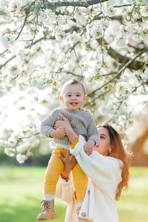 Happy Young Mother With Little Son Walks In Blooming Garden Mom With 1
