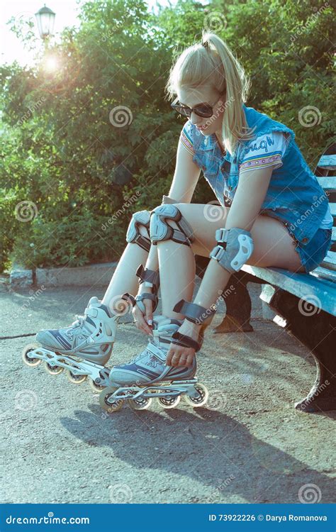 Girl On Rollerblades Sitting On A Bench In A Park And Putting On Inline Skates In A Sunny Bright