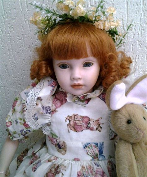 A Doll With Red Hair Sitting Next To A Teddy Bear And Wearing A