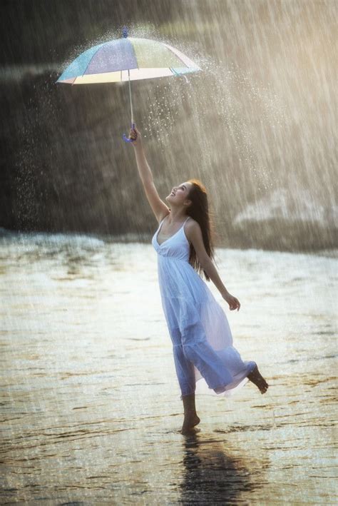 a woman in white dress holding an umbrella over her head while standing in the rain