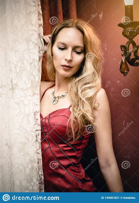 Young Beautiful Woman In An Elegant Red Dress Is In A Room
