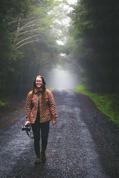 A Young Woman Walking On A Road Through A Forest Filled With Fog And