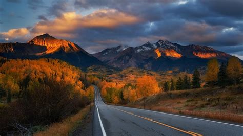 Download Wallpaper 1366x768 Road Trees Mountains Autumn Clouds
