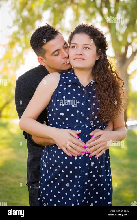 Happy Hispanic Man Hugs His Pregnant Wife Outdoors At The Park Stock