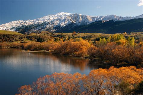 River With Trees Near Mountain Range Covered In Snow During Daytime