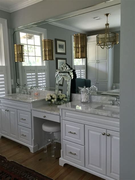 Bathroom lighting is an integral part of your daily life. White cabinets, Carrara marble, brushed gold light ...
