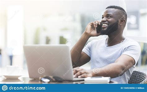 Cheerful African Guy Talking By Cellphone While Typing On Laptop Stock Photo Image Of Business