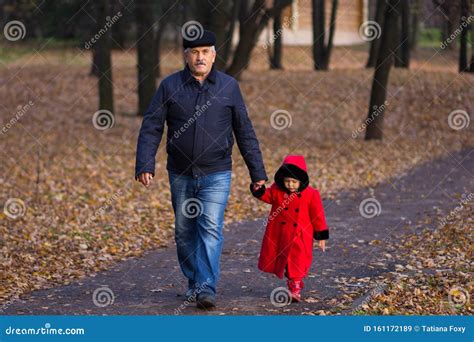 Hombre Maduro Y Niña Cogiendo La Mano Caminando En El Parque Del Otoño