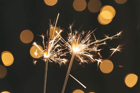 Two Sparklers Are Lit On A Blurred Background Of A Glowing Garland