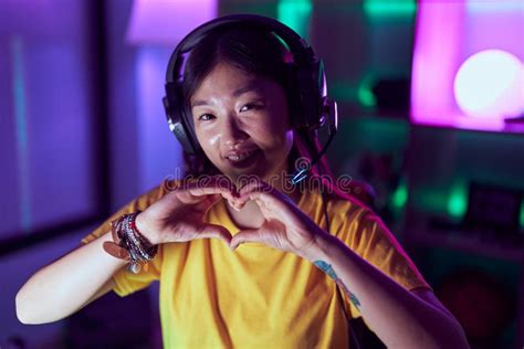Chinese Woman Streamer Using Headset Doing Heart Gesture With Hands At Gaming Room Stock Photo