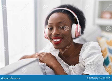 African American Woman Listening To Music Sitting On Sofa At Home Stock