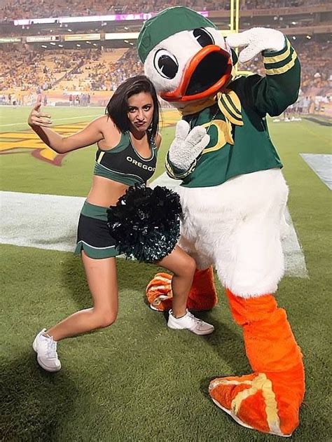 two cheerleaders pose with a duck mascot on the field at a football game