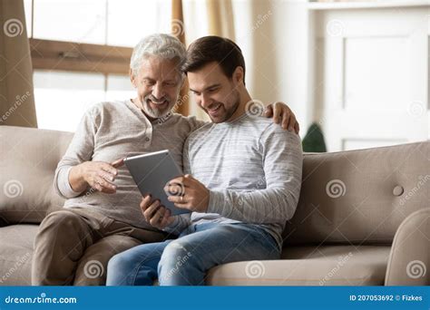 Papá Viejo Y Hijo Adulto Sonriente Usan Tableta En Casa Foto De Archivo
