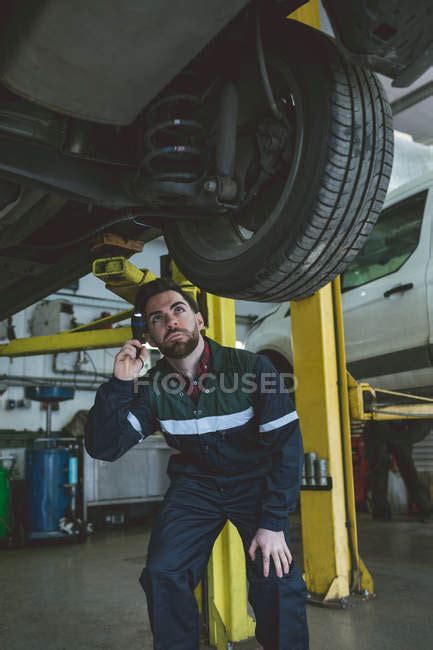 Male Mechanic Examining A Car With Torch In Repair Garage — Auto Repair