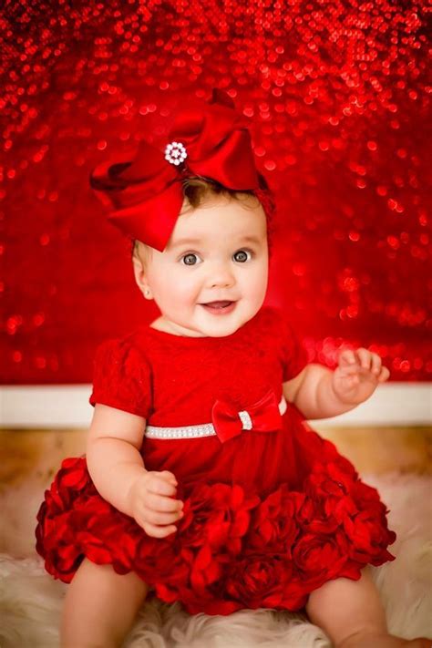 A Baby Girl Wearing A Red Dress With A Big Bow On Her Head And Smiling