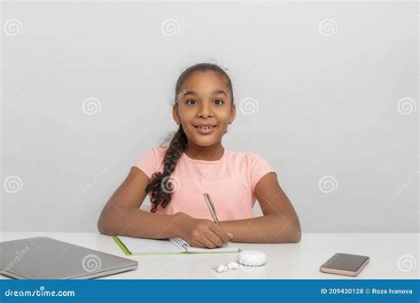 Portrait Of The Schoolgirl Siting At The Table Indoors And Writes Down