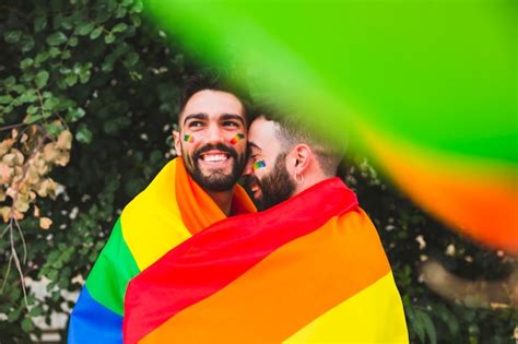 pareja gay con bandera arcoiris abrazando en la calle foto gratis