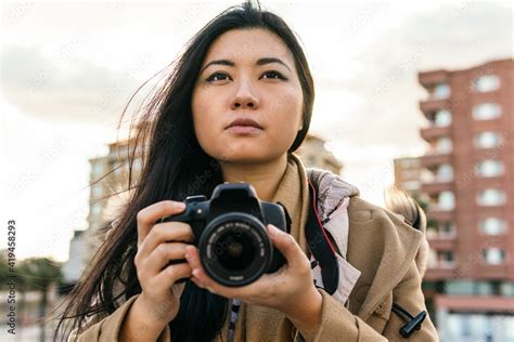 ethnic asian female photographer shooting photo on professional photo camera on city street