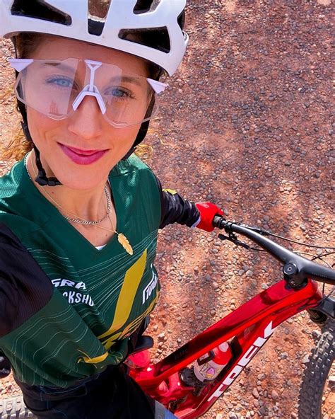 A Woman Wearing A Helmet And Goggles Standing Next To A Bike In The Dirt