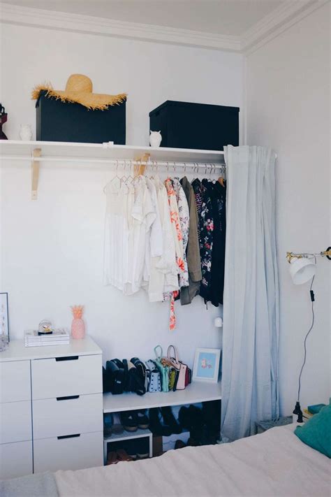 A Bedroom With White Walls And Clothes Hanging On The Rack In Its Corner