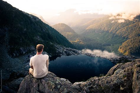 Young Man In White Shirt Sitting On Edge Of High Mountain Cliff