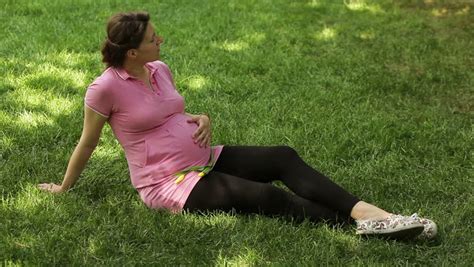 A Pregnant Woman Walks Barefoot On The Grass Holds His Hands On His