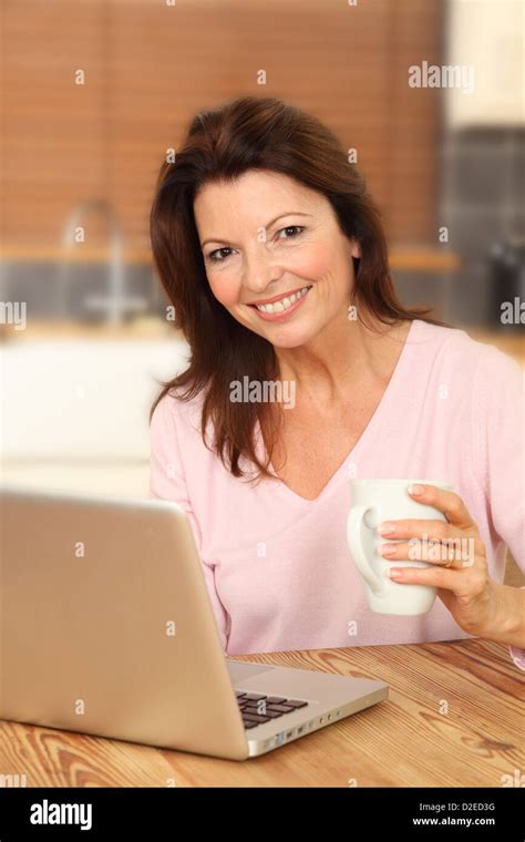 Attractive Mature Woman Using A Laptop Sitting At The Kitchen Table