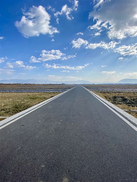 Straight Asphalt Road Under Blue Sky And White Clouds Background And
