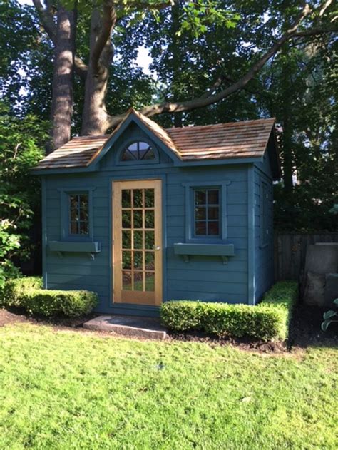 A Small Blue Shed Sitting In The Middle Of A Lush Green Yard Next To A Tree