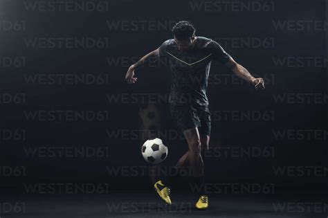 Full Length Of Soccer Player Kicking Ball Against Black Background