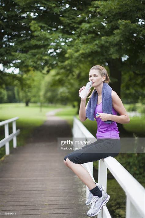 Young Woman Sitting On Bridge After Running And Drinking Water From